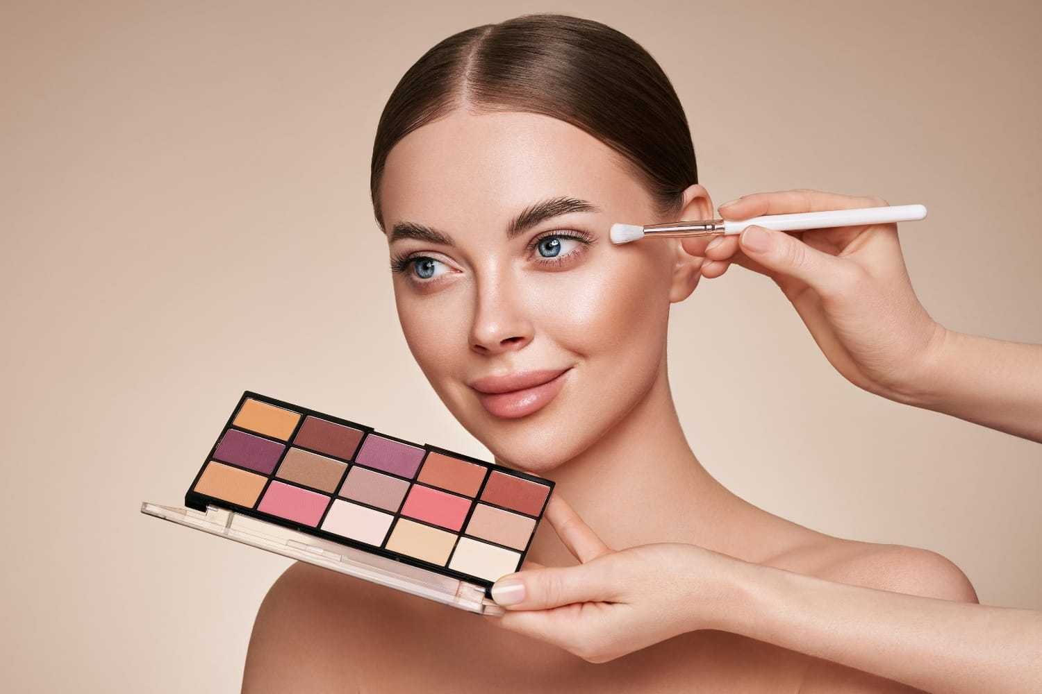 Woman getting eyeshadow applied with makeup palette and brush.